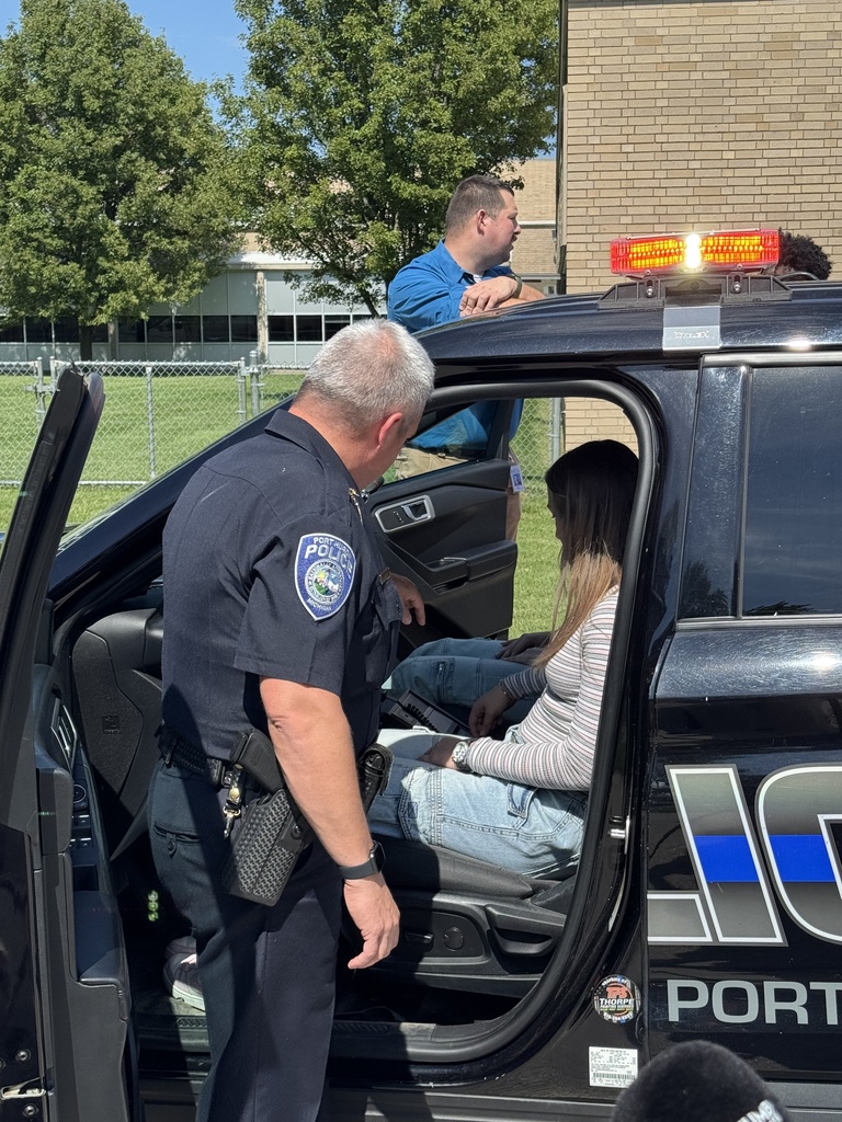 Port Huron Police Chief Brian Kerrigan stands next to the open door of the newly donated retired police cruiser showing the vehicle's equipment to  two students seated in the front seats