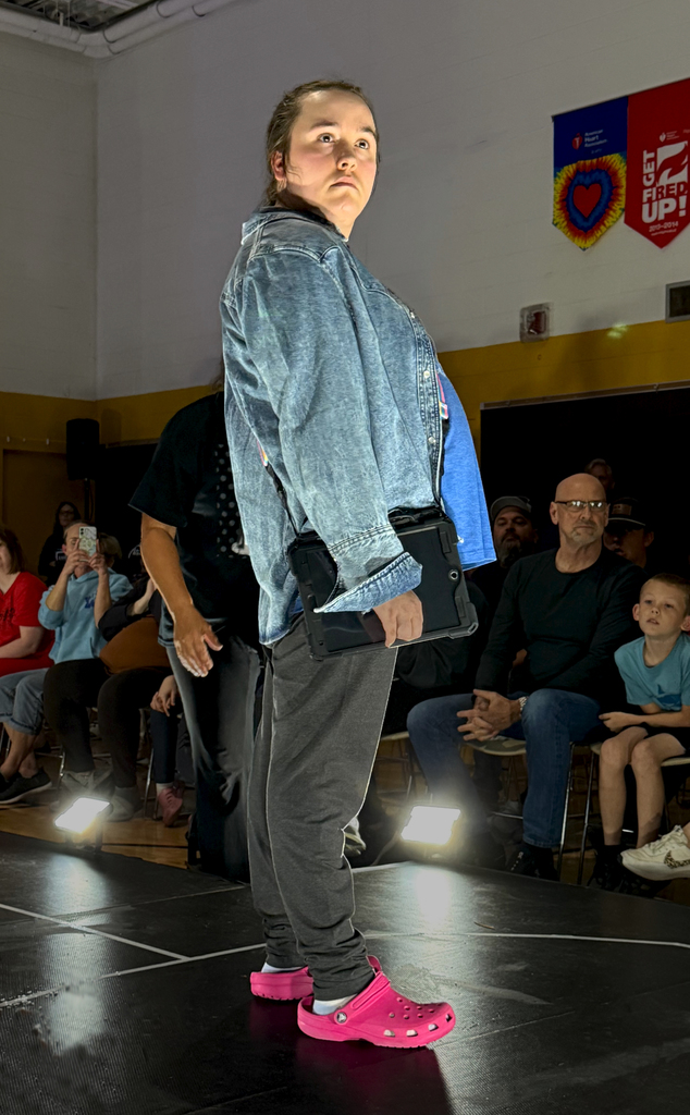 A Woodland student modeling a denim shirt, athletic pants, and Crocs poses at the end of the runway during Fash Bsh