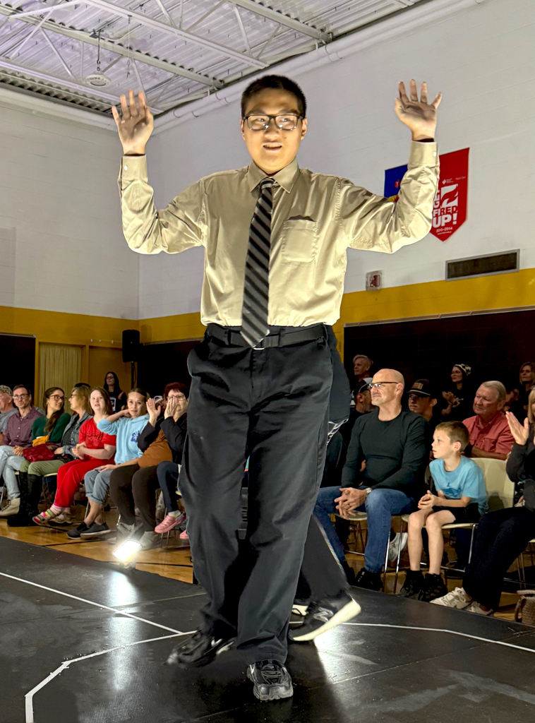 A Woodland student modeling a dress shirt, tie, and dress pants smiles as he poses with his arms in the air.