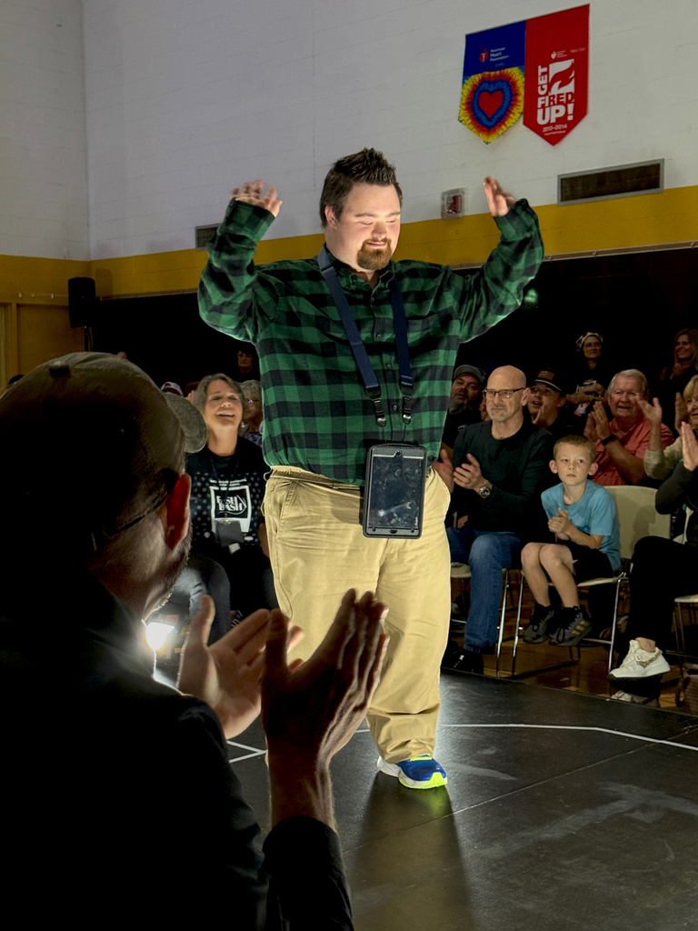 A woodland student wearing a checked shirt and khakis and his hands in the air, walks the runway at the first-ever Fash Bash
