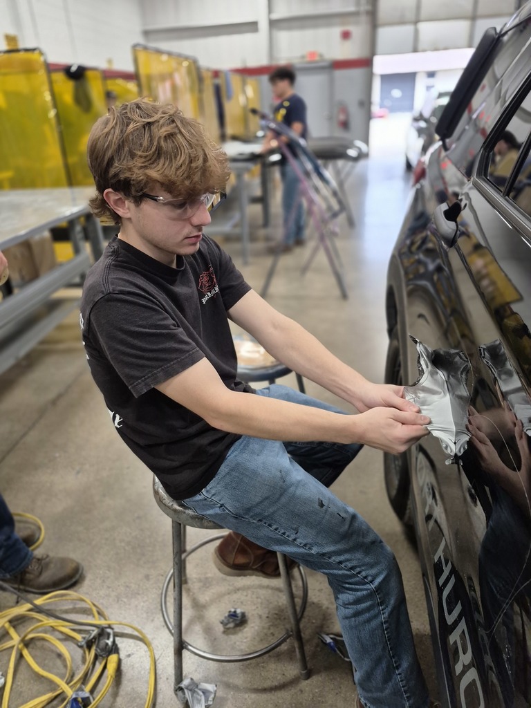 A Collision Repair students pulls a decal off of the recently donated Port Huron Police cruiser