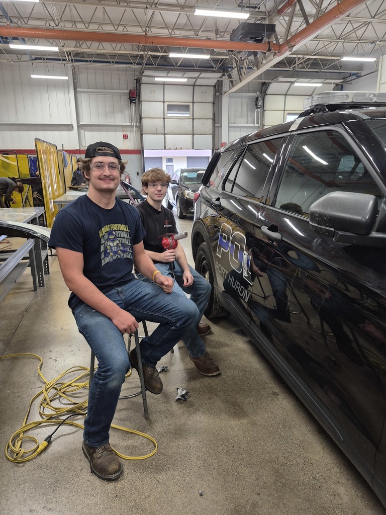 Two Collision Repair students sit next to the recently donated Port Huron Police Cruiser