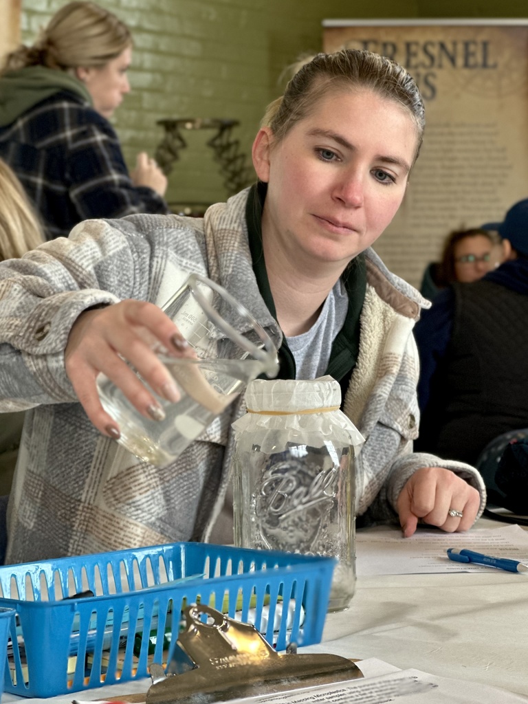 A participant concentrates while pouring lake water through a filter into a mason jar to capture visible microplastics. 