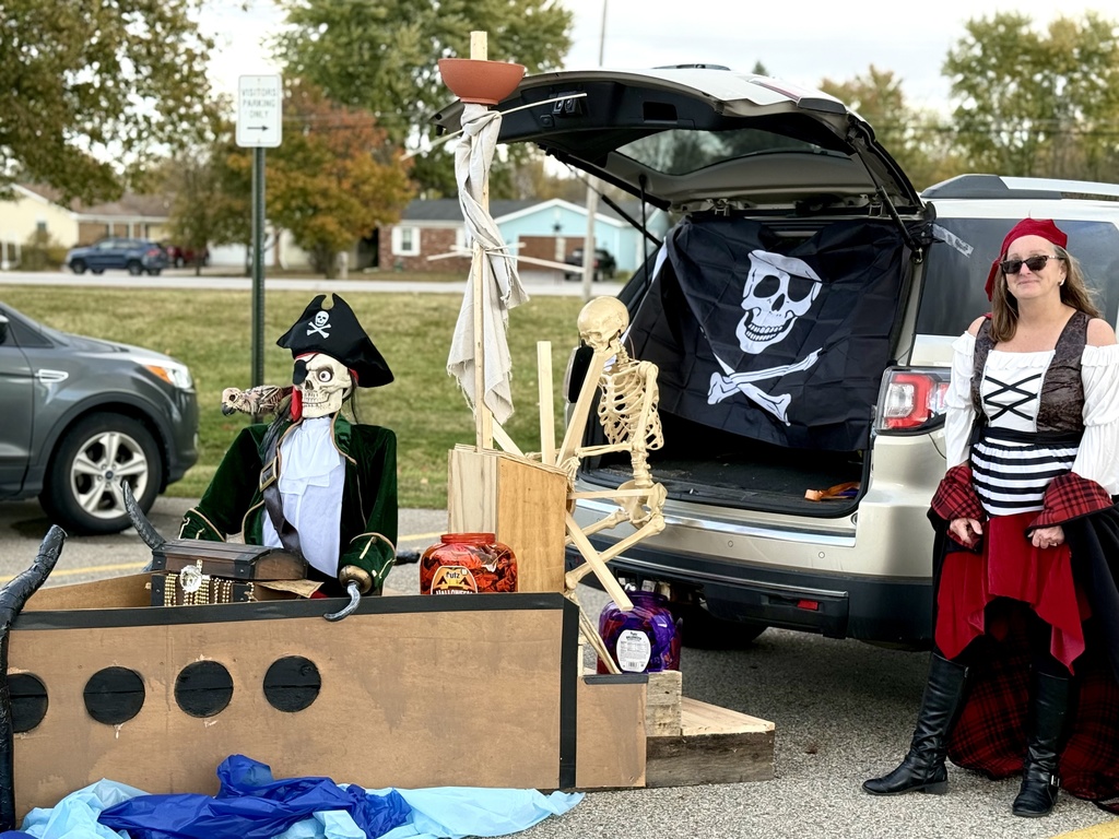 A pirate-themed car setup with skeleton pirates and a treasure chest, with a woman dressed as a pirate standing nearby.