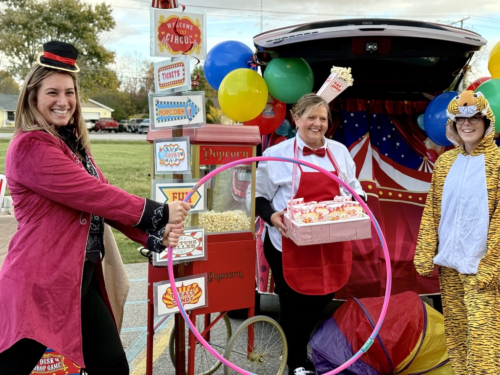 Three people dressed as circus performers (one in a ringmaster costume, one in a popcorn vender costume, and one in a tiger costume) standing in front of a circus-themed trunk.