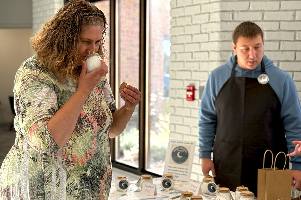 A customer smells one of the Bright Abilities candles at the display table while a student stands nearby ready to assist.