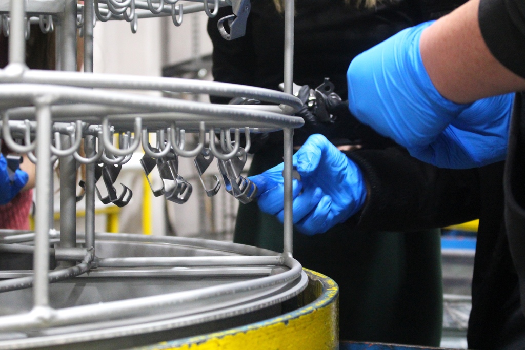 Students at Michigan Metal Coatings hang metal parts to prepare them to be primed and coated 