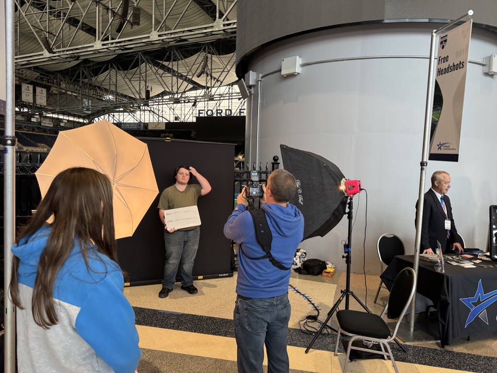 A TEC student holds a placard while being photographed at the Great Lakes Broadcast and Sport Media Acadmey