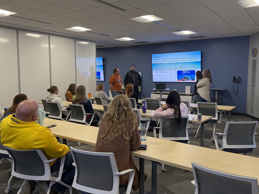 A team of four educators stand in front of display monitor as they present to a group of peers 