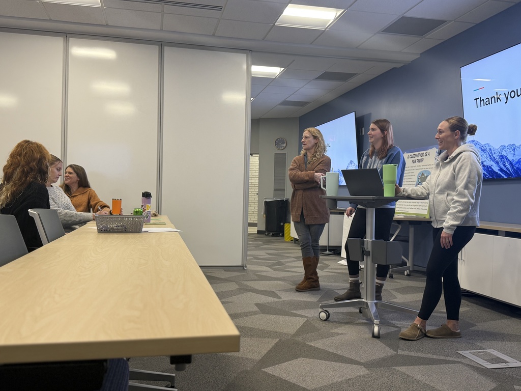 A team of three educators stand in front of a display monitor as they present to a group of peers 