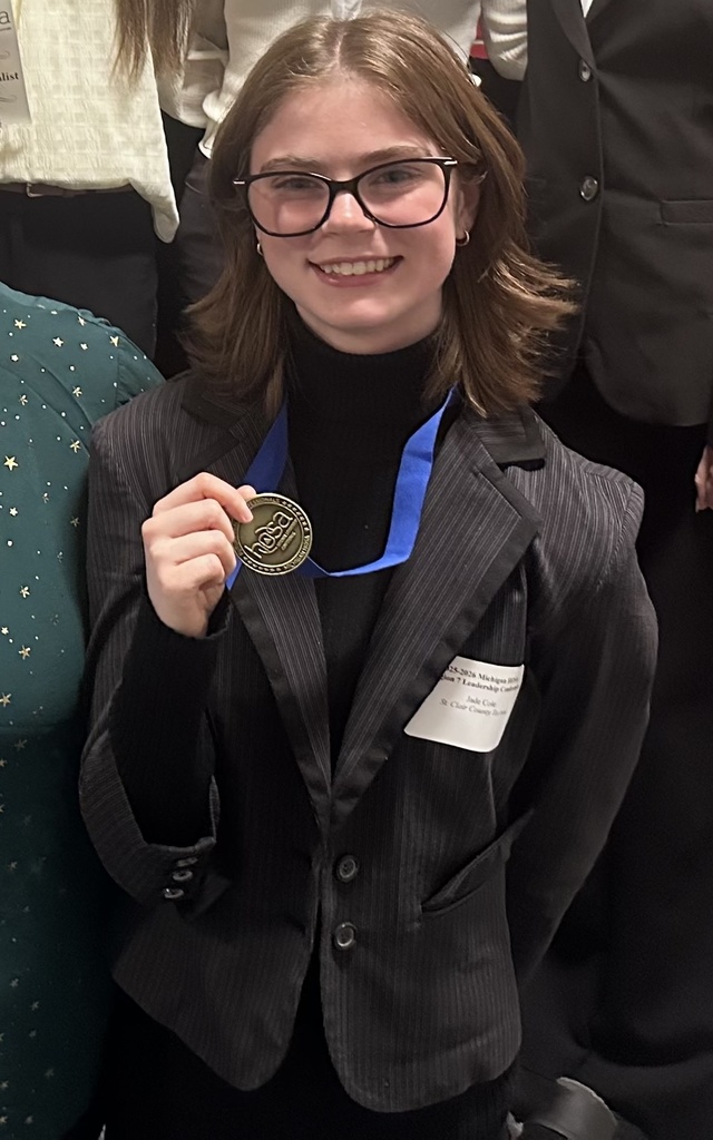 TEC student Jaden Cole wearing glasses and a pin stripe suit smiles while holding up a gold HOSA medal with a blue ribbon.