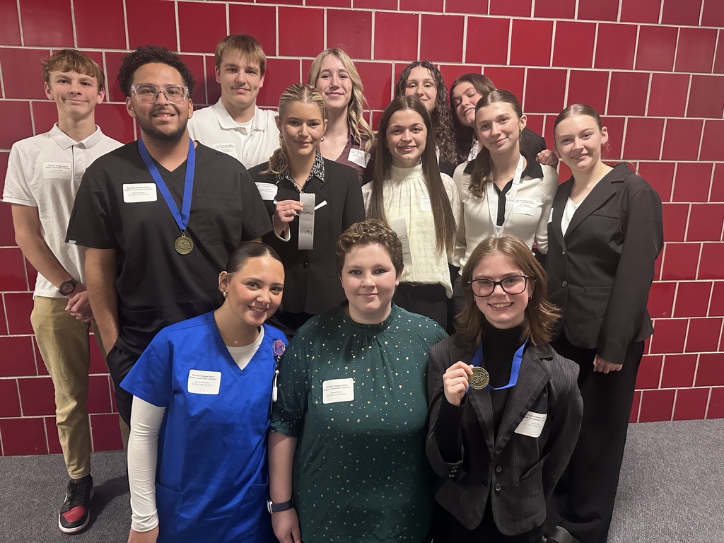 Thirteen Health Careers TEC students pose together against a red-tiled wall, smiling. Some hold medals or ribbons from the competition.
