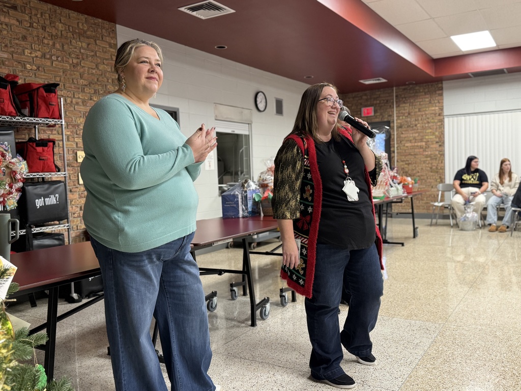 A Woodland teacher wearing a festive sweater speaks into a microphone during the school's annual Holiday Auction