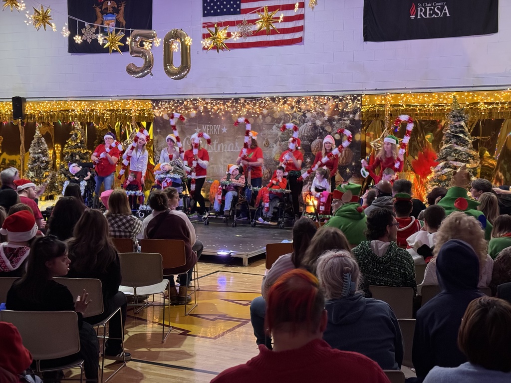 Woodland students dressed in red and white stand on a stage holding oversize candy canes