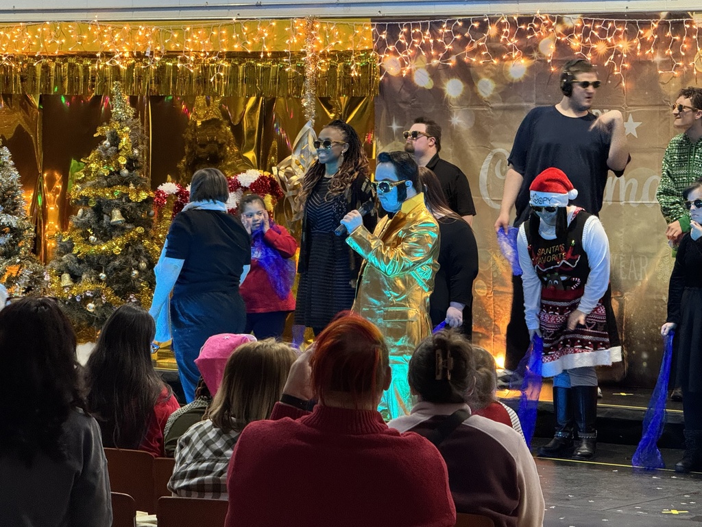 A student dressed in a gold suit sings into a microphone