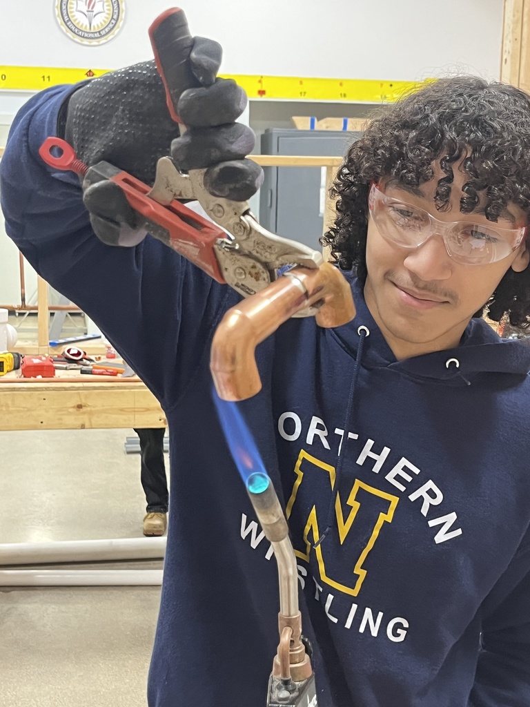 A student wearing safety glasses uses a torch to heat a a copper pipe fitting in a technical lab