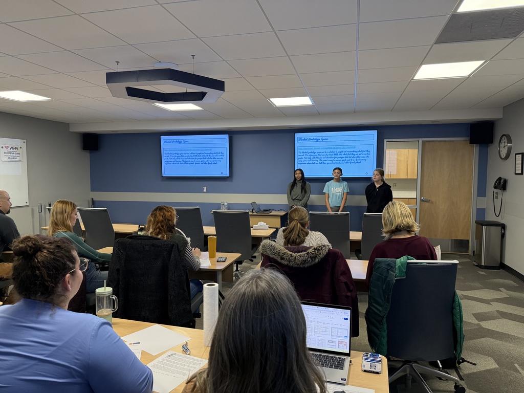 Three students stand in front of a display monitor in a meeting room of adult community members