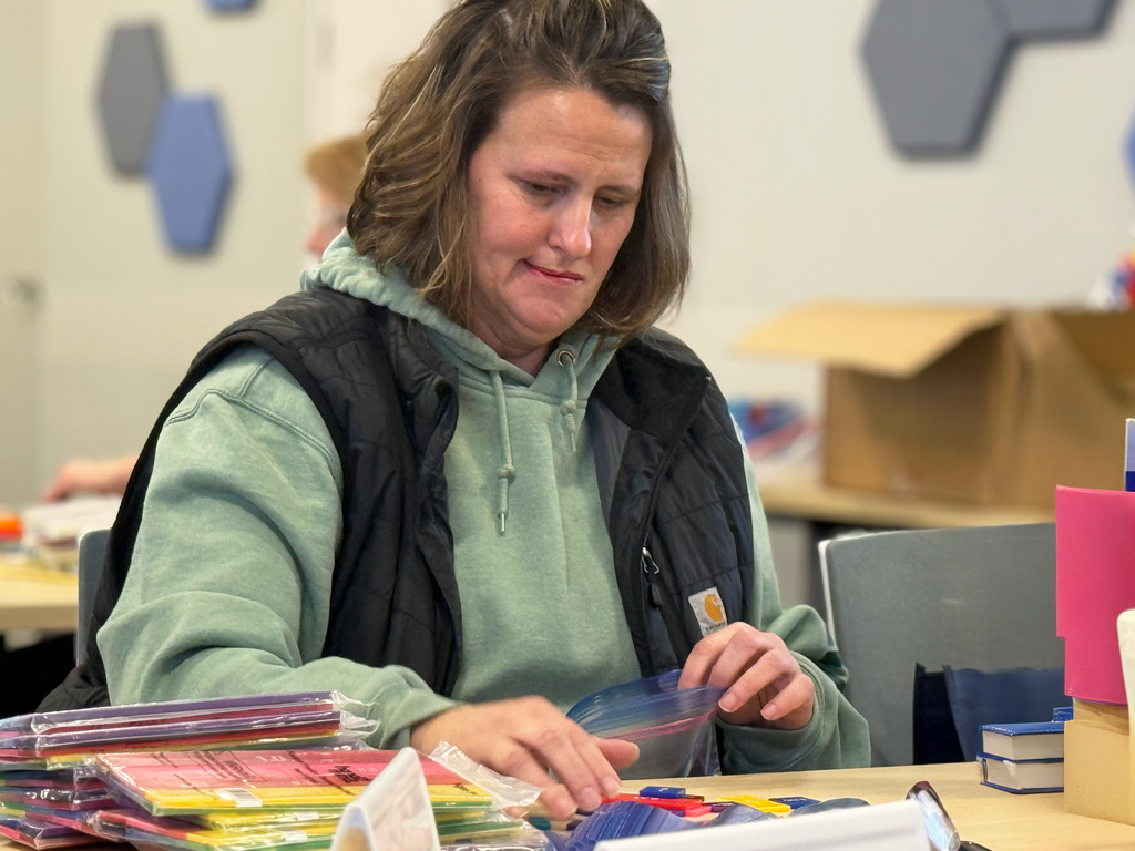 An educator wearing a green shirt and black vest organizes fraction strips at a table during a professional development workshop on fractions.
