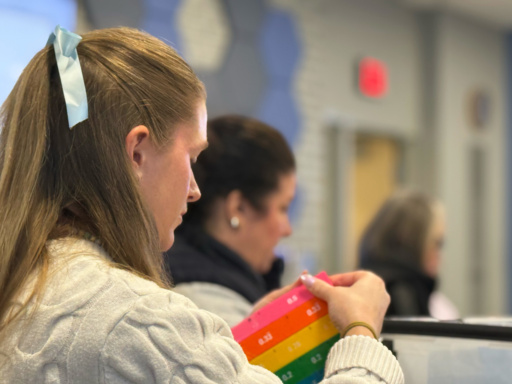 An educator examines colorful fraction strips while other educators work in the background during a professional development workshop on fractions.