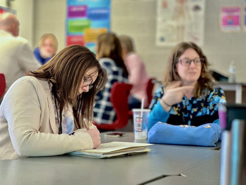 A woman sitting at a table writes in a notebook
