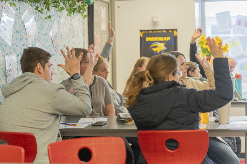 Attendees seated at a table raise their hands in the air