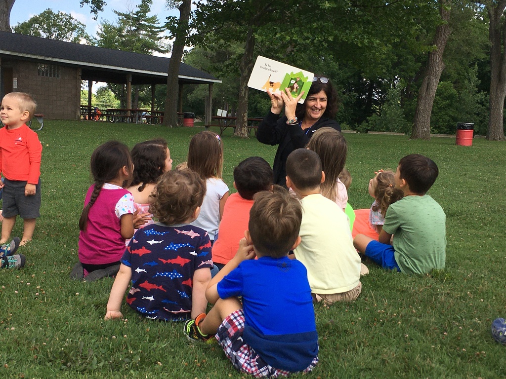 RESA's Jen Gunderson holds up a picture book to a group of toddlers during a playgroup at a local park