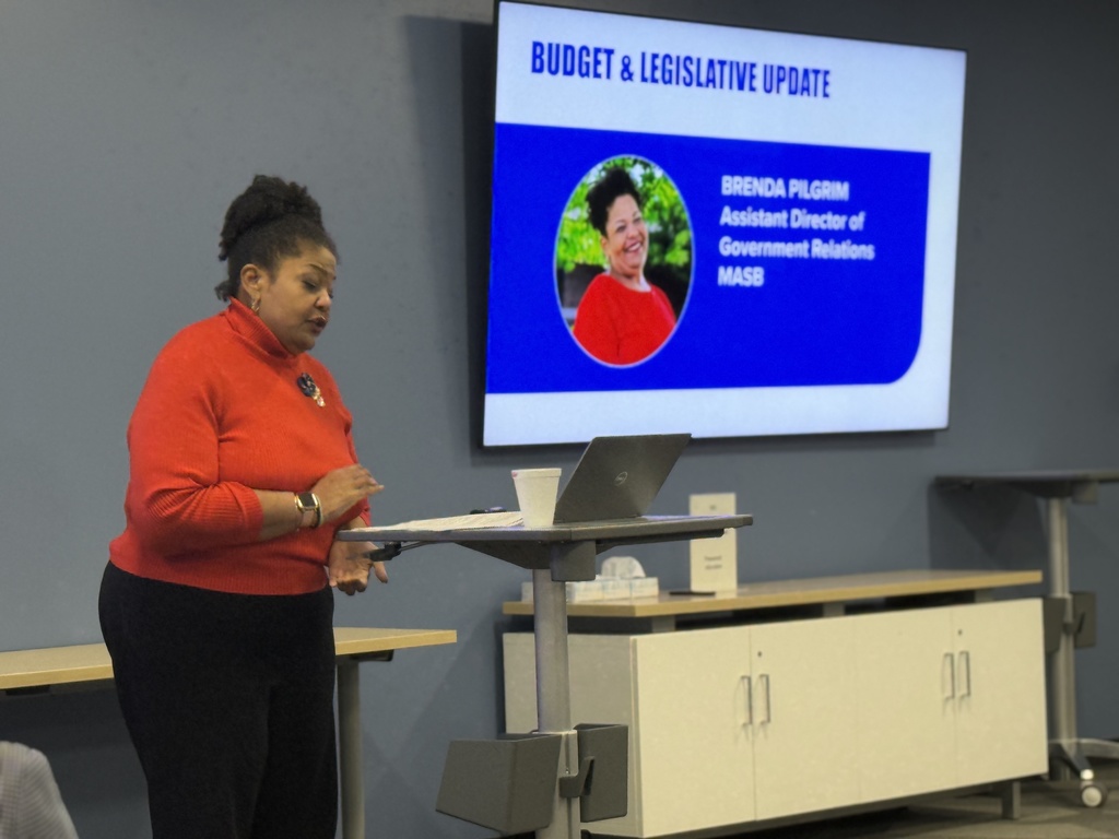 MASB's Brenda Pilgrim at a standing desk with a digital monitor behind her