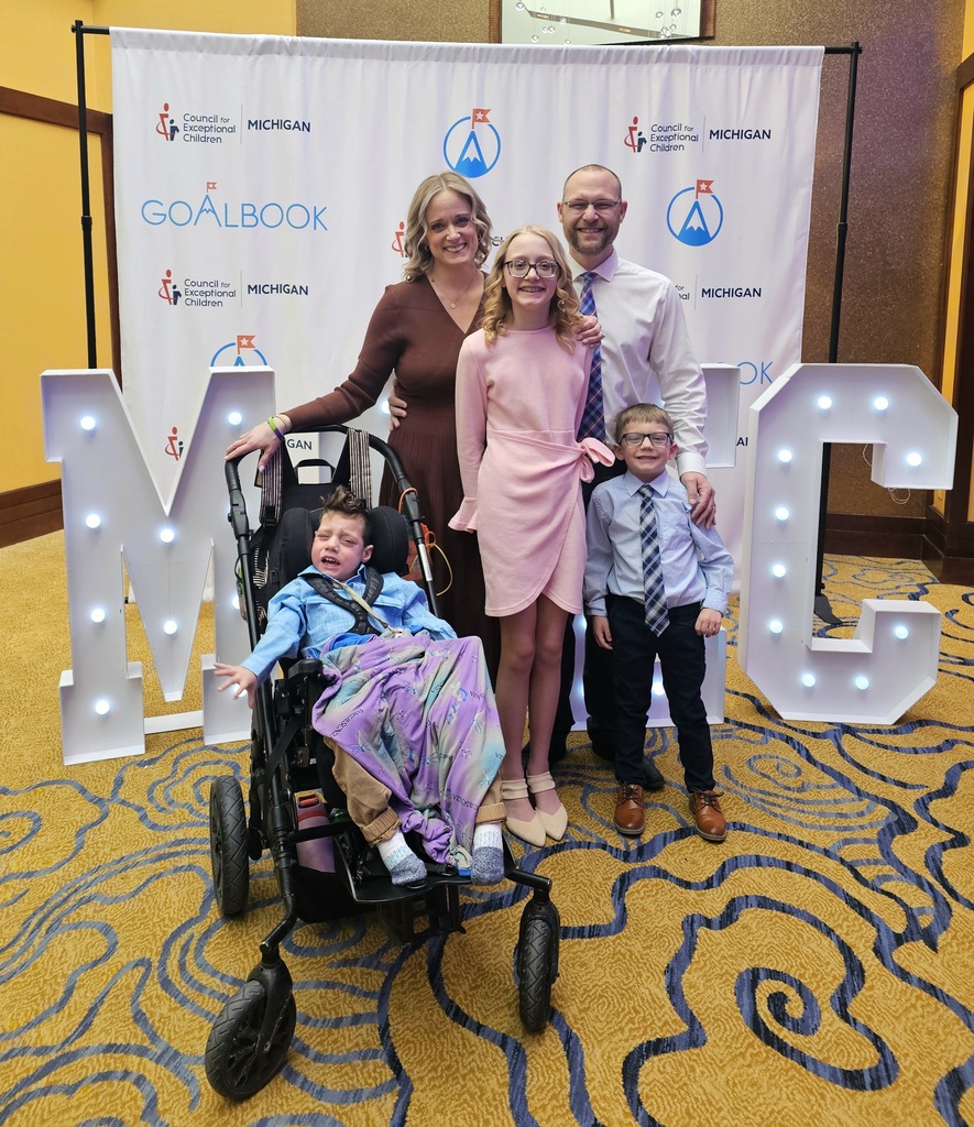 The Krauskopf family of five stands stands in front of a Michigan Council for Exceptional Children awards backdrop. From left to right are Miles seated in a wheelchair, Lindsay, Juliet, Dan, and Elijah.