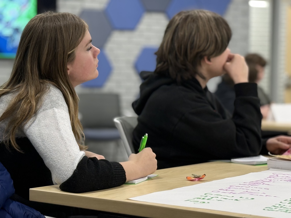 Two students seated at tables take notes during a presentation by the DNR