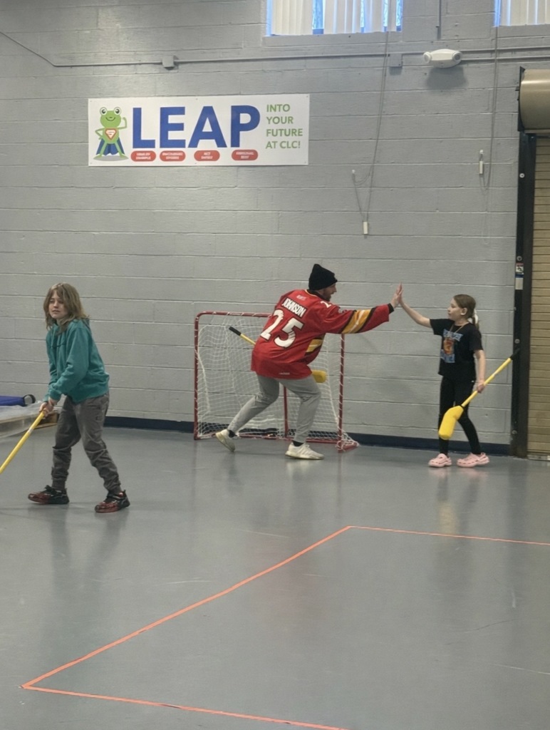 A Prowler play and two students play hockey in the school gym. The player high-fives a student