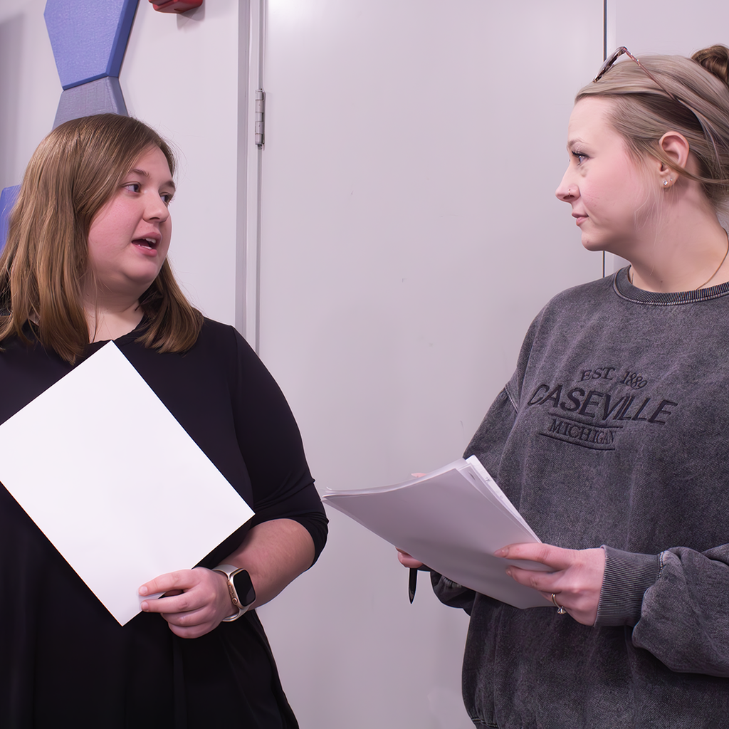Two people holding papers engaged in a conversation