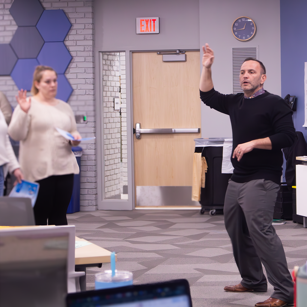 Presenter Joe Zima holding his hand up leads the room in an acitivity