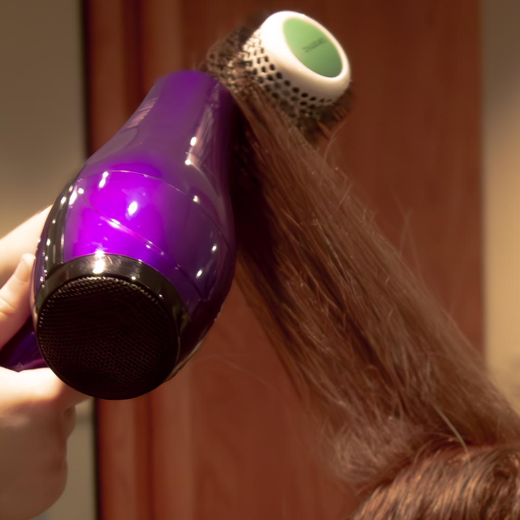 Closeup of a hand holding a hair dryer and brush as they dry a person's long hair