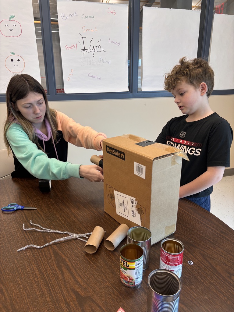 A teacher and student construct a robot from paper tubes, boxes, and cans.