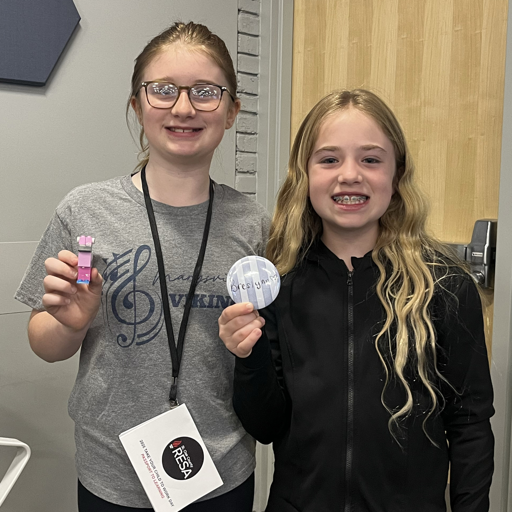 Two students smile at the camera. One holds a LEGO construction and the other holds a name badge they created