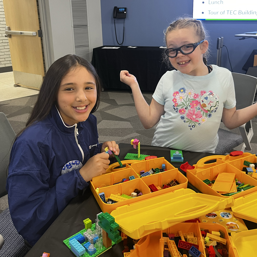 Two student building with LEGOs smile at the camera
