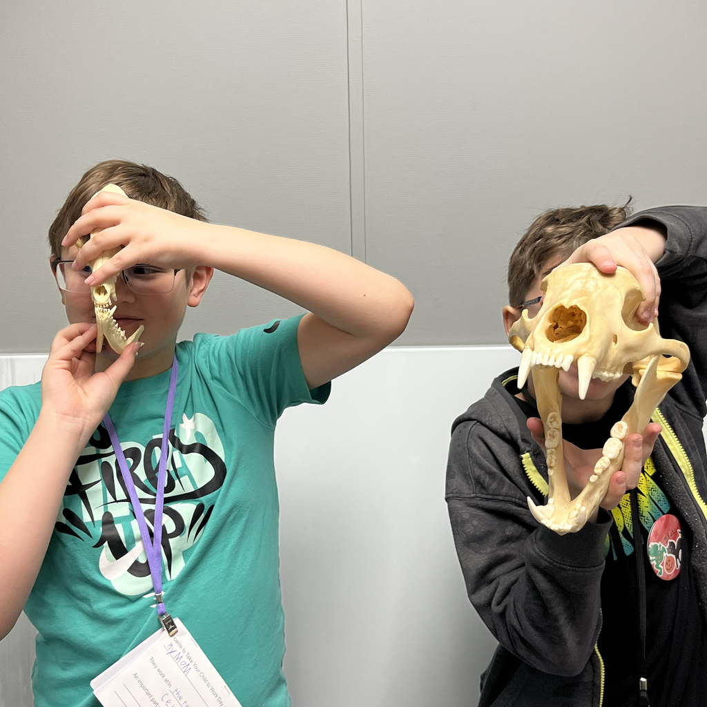 Two students hold animal skulls up to their faces.