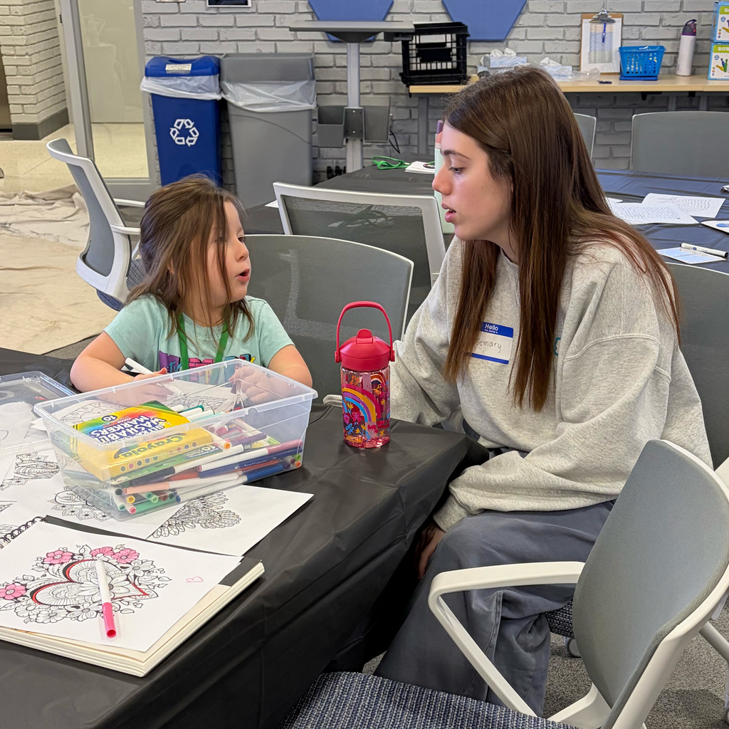 An adult and student sit at a table coloring
