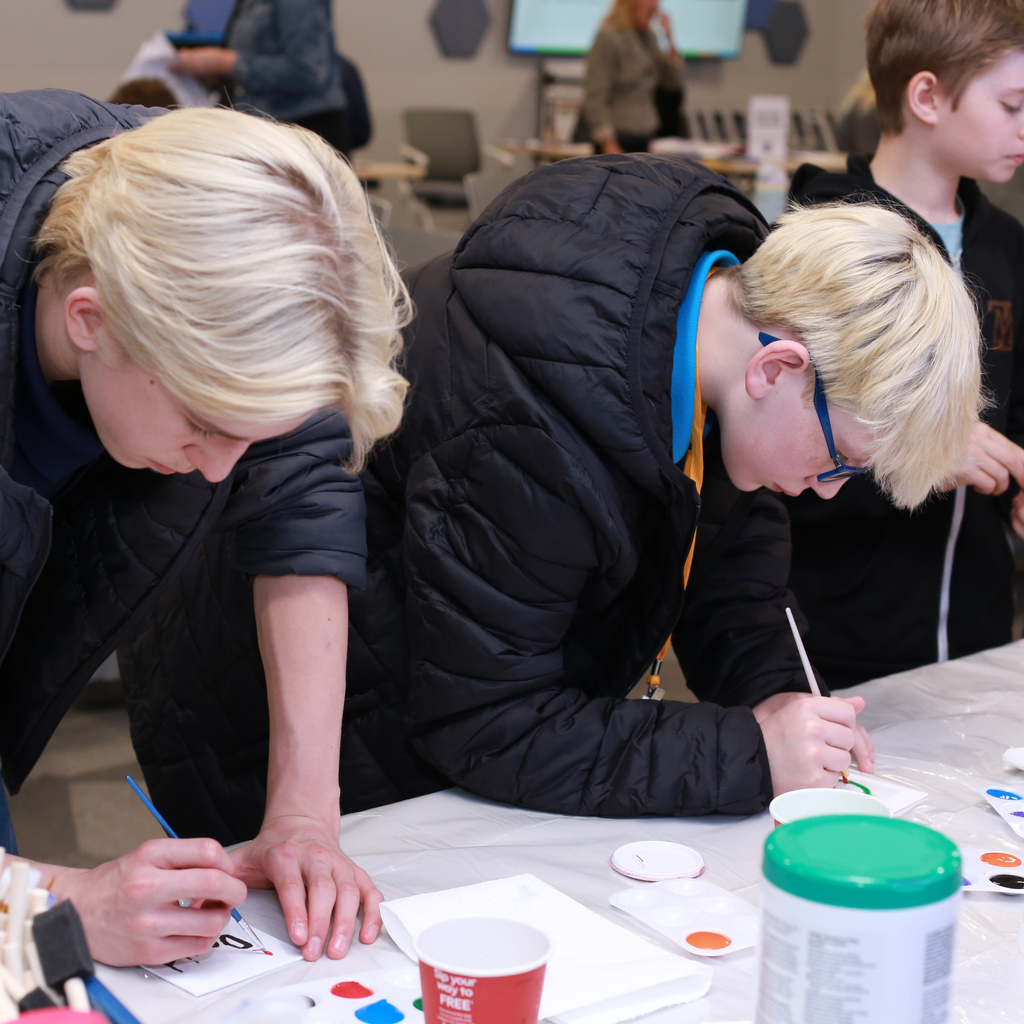Two students lean over a table painting