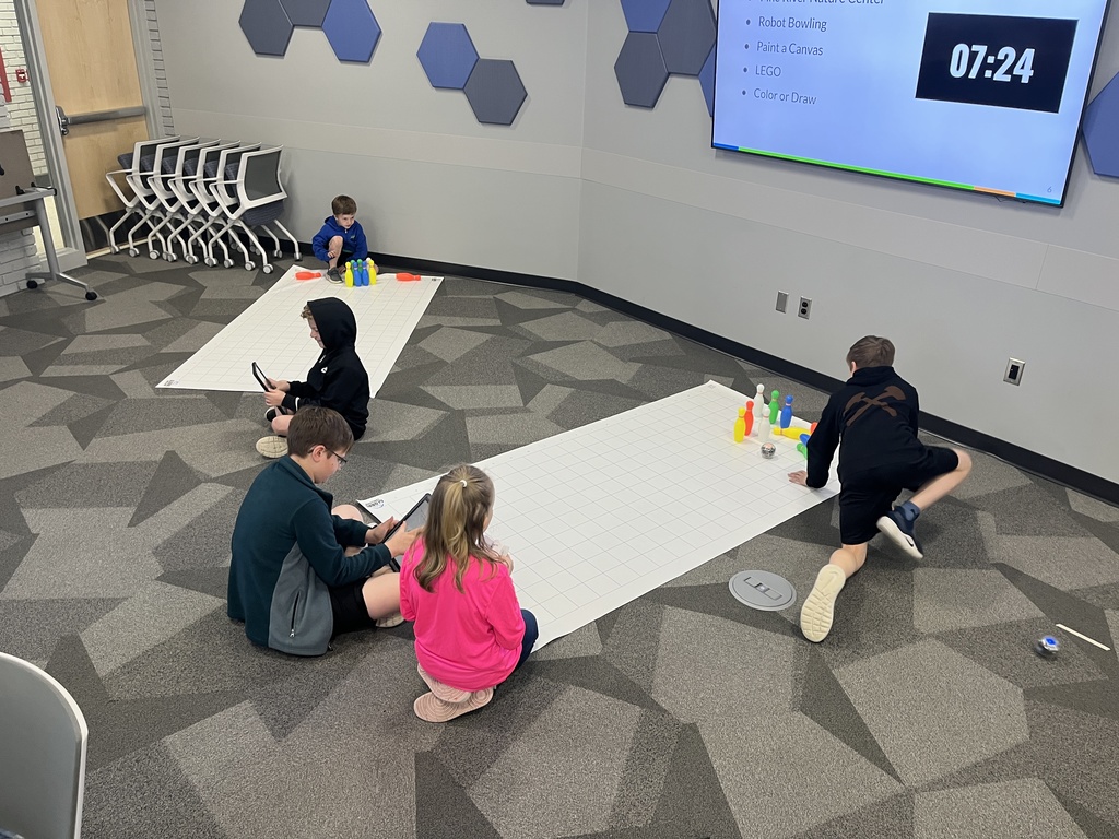 Students sitting on the floor use an iPad to program a robotic bowling game