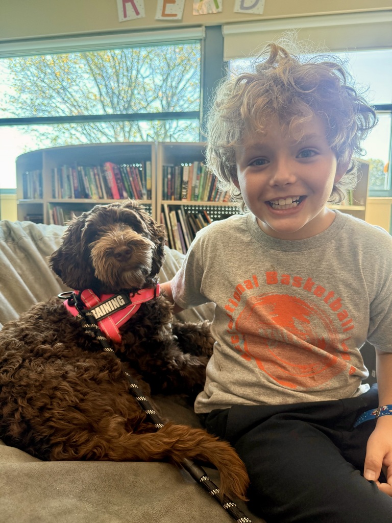 A smiling student poses with their arm around Frannie the therapy dog