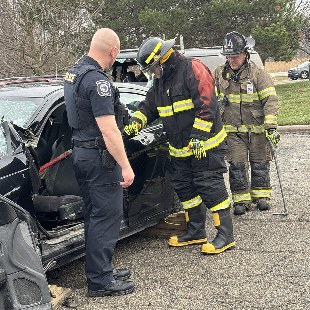 A student inspects a damaged car while two Marysville Public Safety members look on