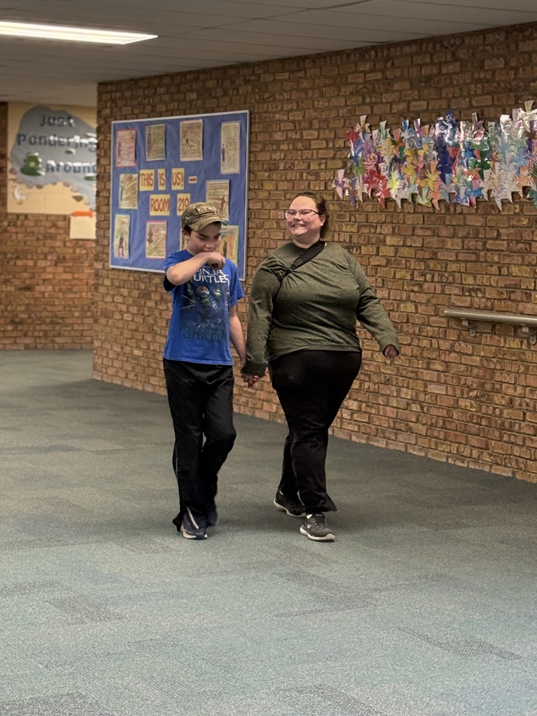 A staff member holds hands with a student while they walk in the school hallway
