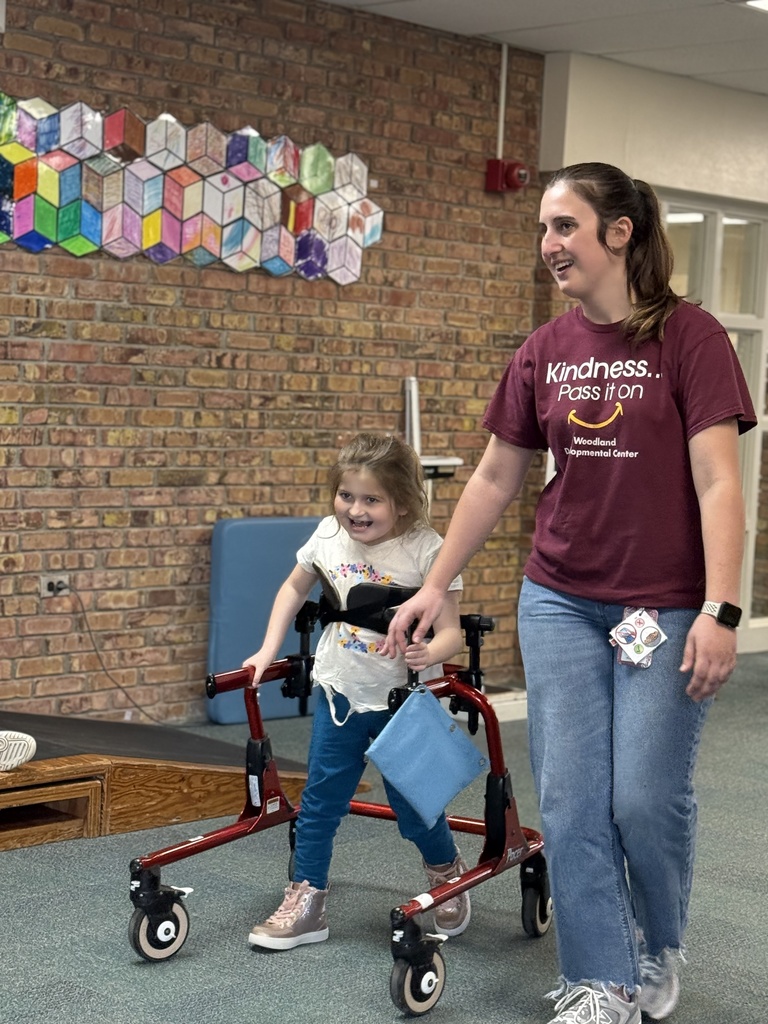 A student using a walker moves independently while a staff member follows nearby