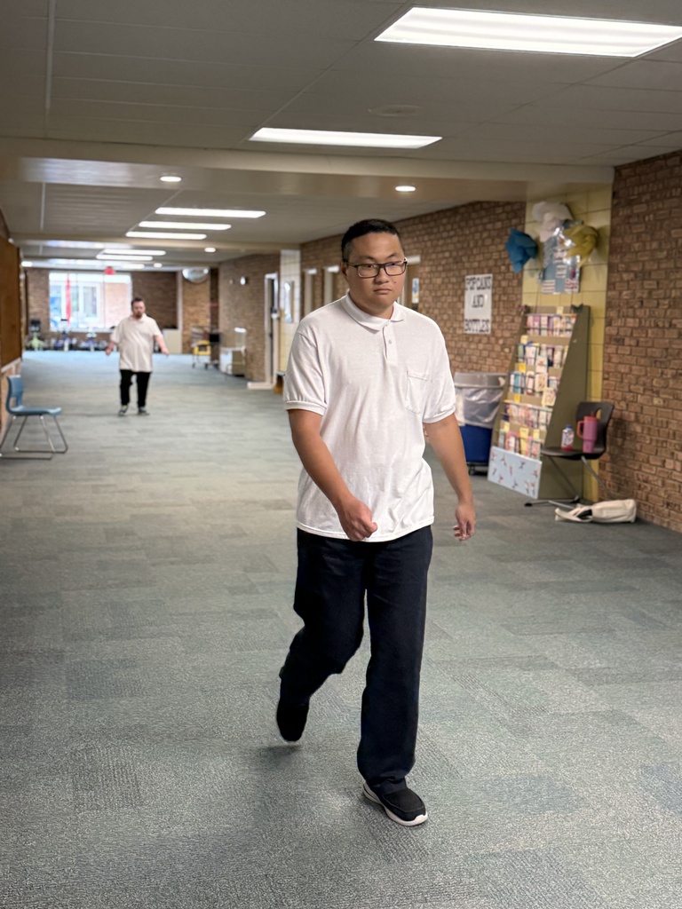 A student walks toward the camera in a hallway while another student walks in the background