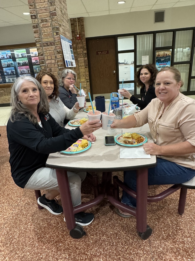 Five TEC staff members raise smoothies together while seated at a cafeteria table during Teacher Appreciation Week