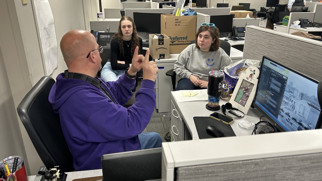Two TEC students listen as a SCCRESA IT staff member explains technology and cybersecurity concepts in an office workspace