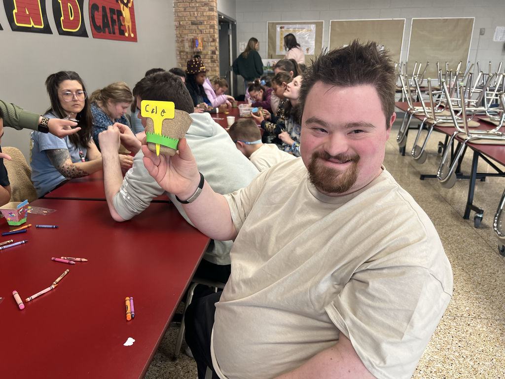 A Woodland Developmental Center student proudly holds up a decorated planter during Garden Club while classmates work in the background.
