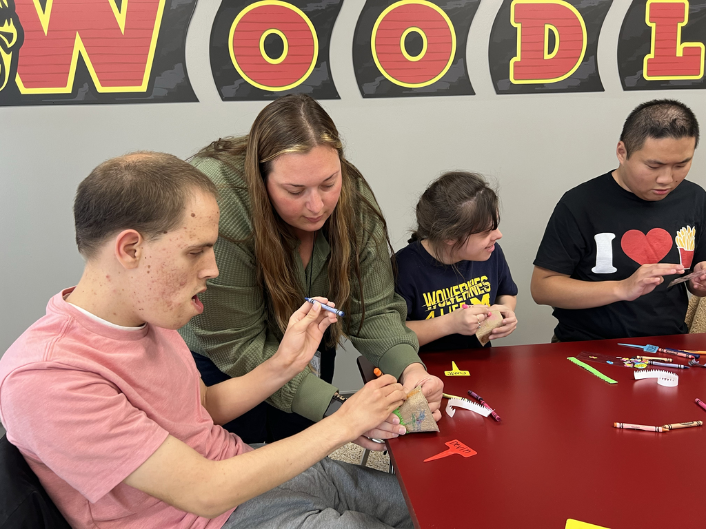 A staff member holds a planter for a Woodland student as they color it