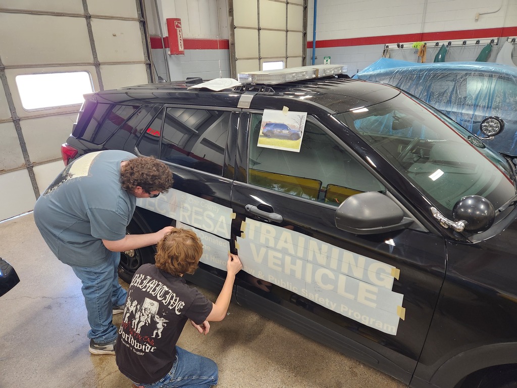 Two Collision Repair students apply decals to a black decommissioned police cruiser inside an automotive lab at St. Clair TEC.